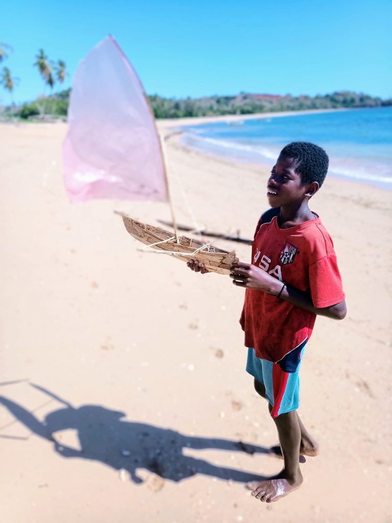 Enfant malgache tenant une pirogue artisanale sur le bord de mer à Madagascar